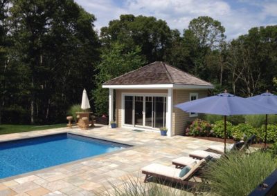 picture of a beautiful pool and pool house with a stone patio and lawn chairs