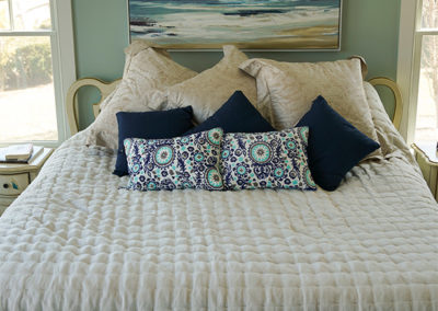 picture of queen size bed with blue bedspread and pillows with ocean picture above- ocean getaway